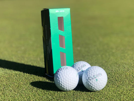 Svart och vitt CLEAR Tour golfbollar från Inhousegolf.se på gräs, visar detaljerad närbild av golfbollarna.